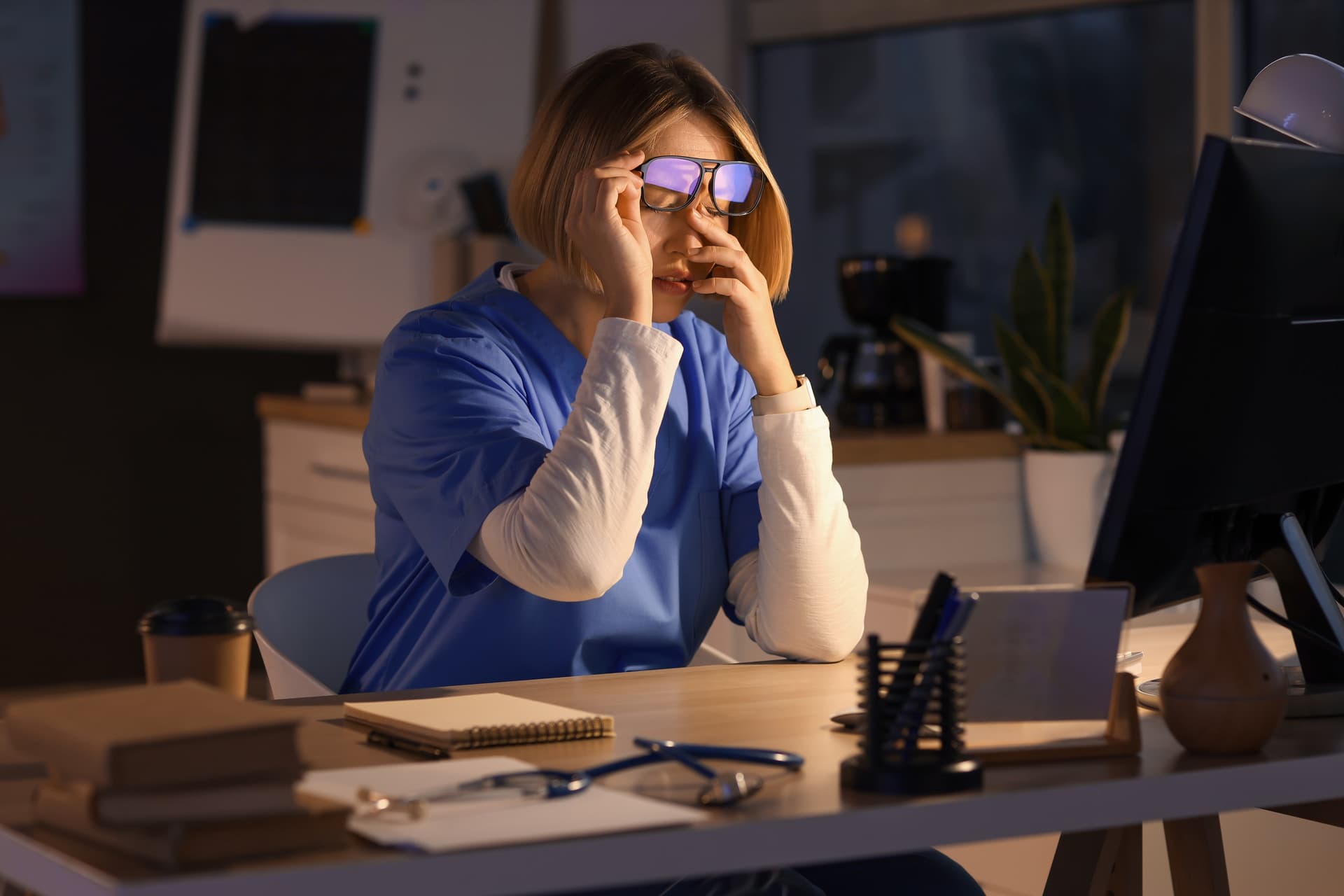 A fatigued healthcare professional reviewing a schedule on a computer screen in a hospital office