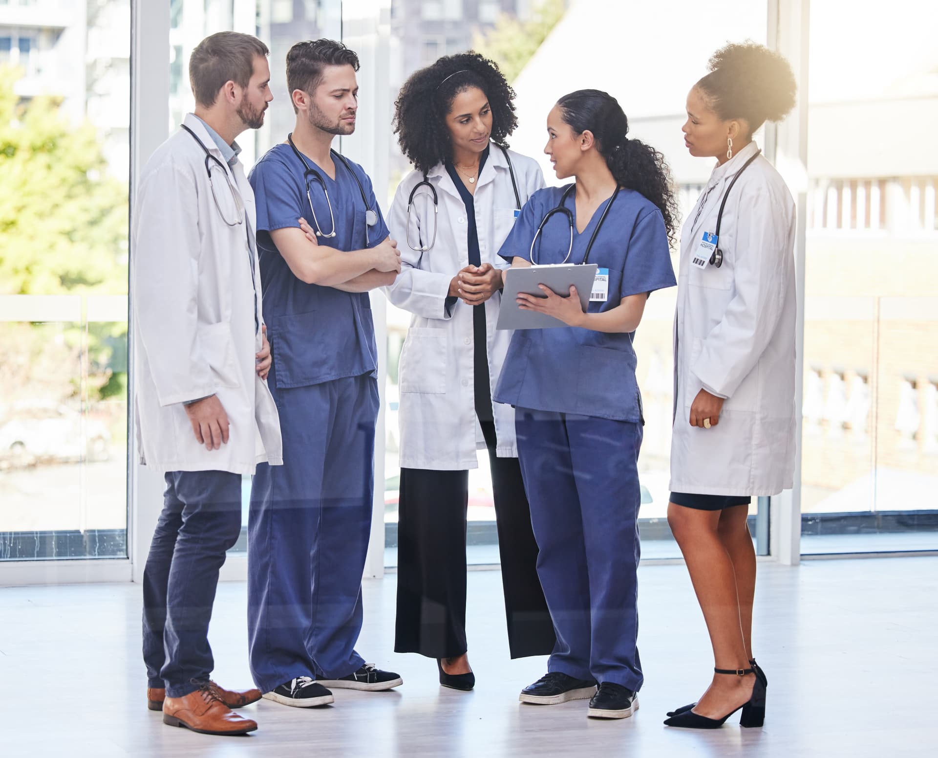 A diverse group of healthcare professionals in a meeting room collaboratively reviewing a schedule displayed on a large screen