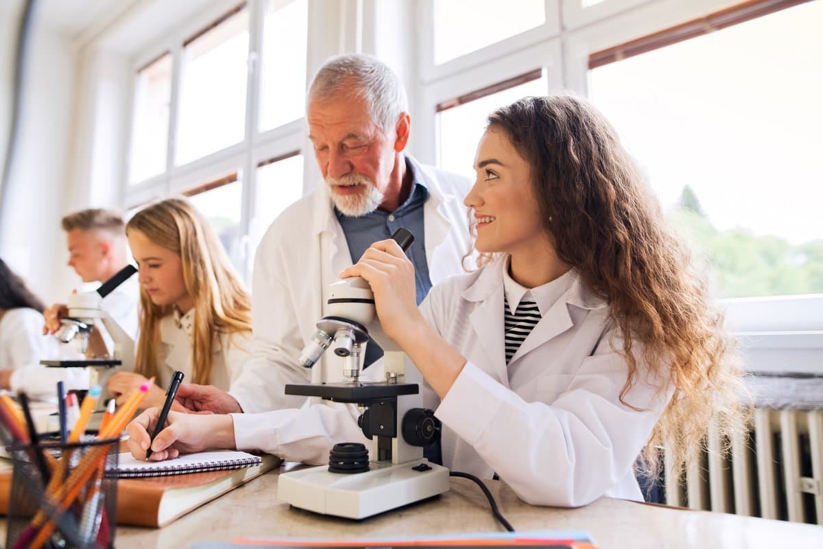 Senior pathologist supervising and mentoring a junior colleague at the microscope