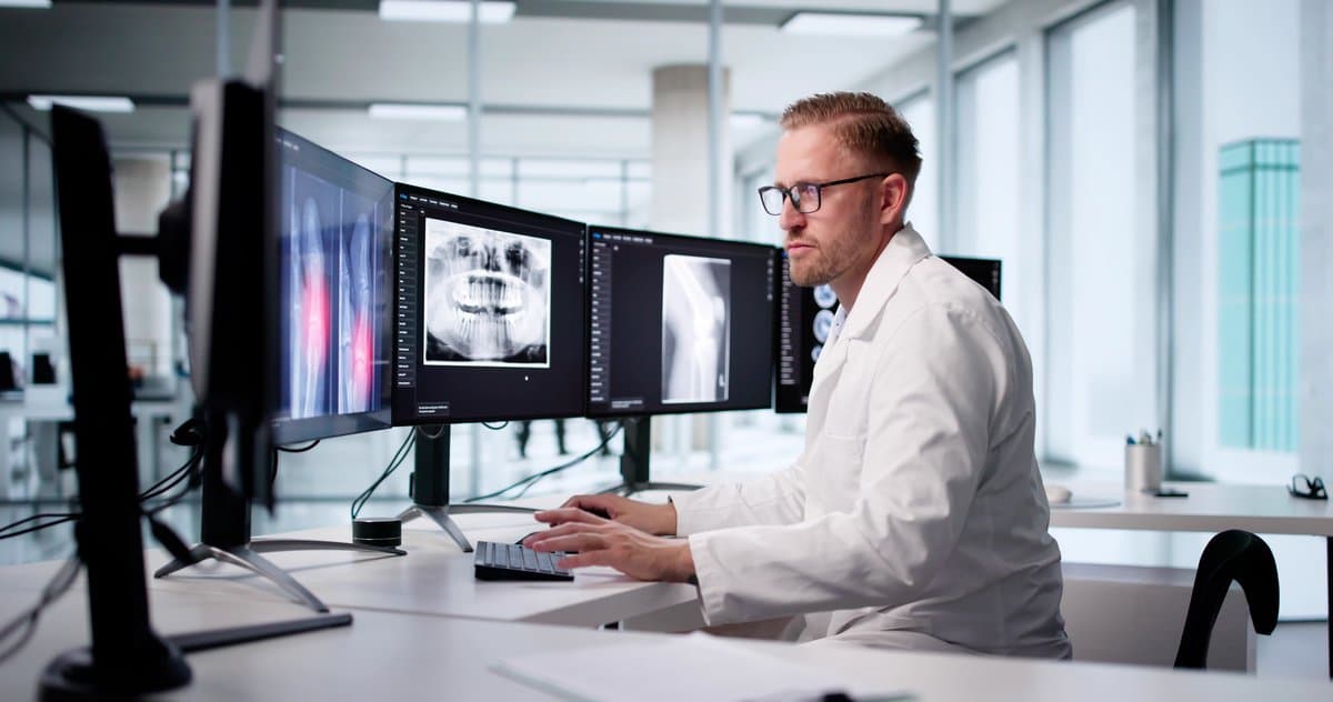 Radiologist reviewing diagnostic imaging scans on multiple monitors in a modern reading room